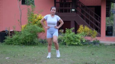 Orta yaşlı bir kadın evinin önündeki çimlerde egzersiz yapıyor..