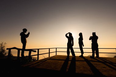 Gün batımında dağda fotoğraf çeken dört turistin silueti..