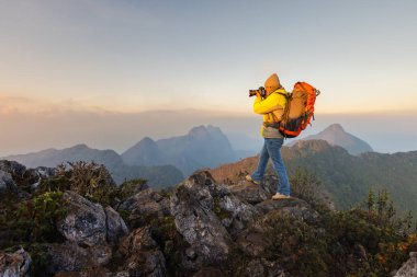 Doğa Fotoğrafçılığı Konsepti. Profesyonel Doğa Fotoğrafçısı dağların tepesinde gün batımında fotoğraf çekiyor. Yürüyüş, fotoğraf çekme, dağ zirveleri.