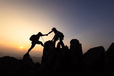 Gün doğumunda bir dağa tırmanmaya yardım eden iki yürüyüşçü. Birbirimize yardım ediyoruz. Tırmanıyorum. Kurtarma ve takım çalışması konsepti. Dağlarda el ele tutuşuyoruz..