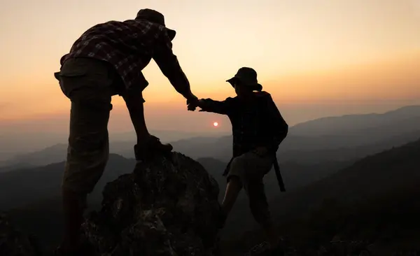 Two hikers helping each other climb a mountain at sunrise. Helping each other. Climbing. Rescue and teamwork concept. Helping hand in the mountains.