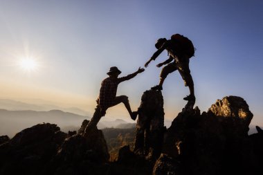 Zirvedeki dağa ve gündoğumu arka plan tırmanma ekibine yardım eden insanların silueti başarılı bir iş konsepti üzerinde çalışıyor. Zirvedeki dağcılar ekibin çalışmasına yardım ediyor..