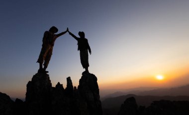 Dağcılardan oluşan bir ekibin silueti engebeli bir dağa tırmanıyor, birlik ve kararlılık sergiliyor, sürekli büyüme ve başarı için bir takım çalışması kültürünü kucaklıyor..