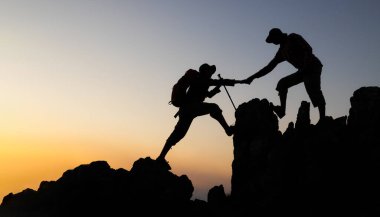 Zirvedeki dağa ve gündoğumu arka plan tırmanma ekibine yardım eden insanların silueti başarılı bir iş konsepti üzerinde çalışıyor. Zirvedeki dağcılar ekibin çalışmasına yardım ediyor..