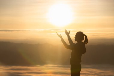 Silhouette of a woman praying on a mountain at sunrise. Young woman praying to God. clipart