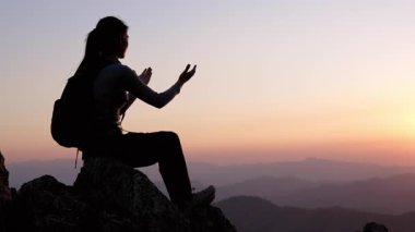 Günbatımı kavramında elleri havada bir kadının silueti dine ibadet ve övgü için. Dua eden ve meditasyon yapan genç bir kadın. Kişisel bakım ve farkındalık, duanın gücü.
