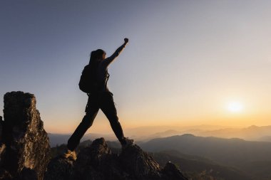 Gün doğumunda sisli dağlara ve bulutlara tepeden bakan, zafer içinde kollarını kaldırmış, dağın tepesinde duran bir insanın silueti. Başarı ve hedefe ulaşma. Halk başarısı