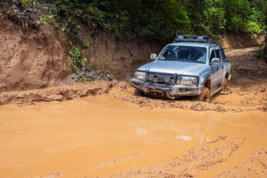 Çamurlu bir yolda giden bir off-road aracı. Engebeli bir arazide toz ve kiri tekmeleyen bir off-road aracının tekerine yakın çekim..