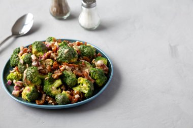 Ev yapımı Brokoli Bacon Salatası gri arka planda, yan manzaralı bir tabakta. Metin için boşluk.