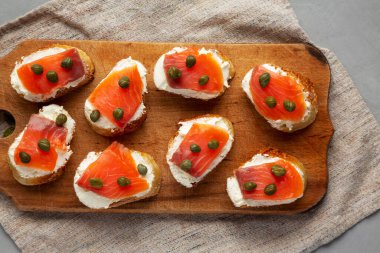 Ahşap bir tahtanın üstünde ev yapımı füme ve krem peynirli crostini. Dümdüz, tepeden, yukarıdan.