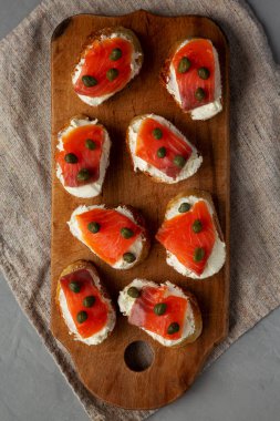 Ahşap bir tahtanın üstünde ev yapımı füme ve krem peynirli crostini. Dümdüz, tepeden, yukarıdan.