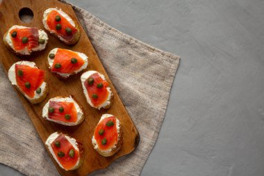 Ahşap bir tahtanın üstünde ev yapımı füme ve krem peynirli crostini. Dümdüz, tepeden, yukarıdan. Boşluğu kopyala.