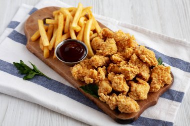 Homemade Popcorn Chicken with BBQ Sauce on a Rustic Wooden Board, side view. 