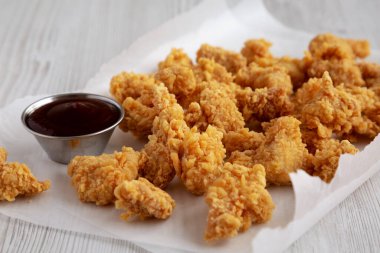 Homemade Popcorn Chicken with BBQ Sauce on a white wooden background, side view.