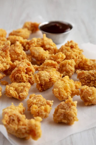 Homemade Popcorn Chicken with BBQ Sauce on a white wooden background, side view.