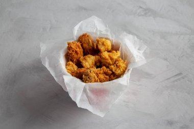 Chicken popcorn, wings, tenders in paper box on a gray background, side view. 