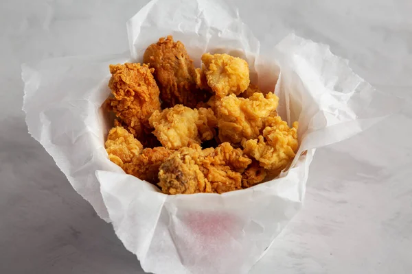 Chicken popcorn, wings, tenders in paper box on a gray background, side view. Close-up.