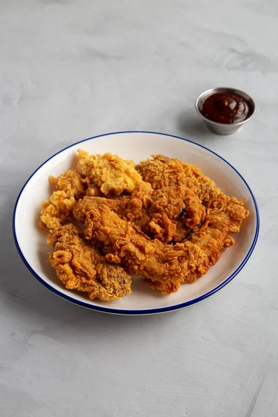 Chicken Popcorn, Wings and Tenders with BBQ Sauce on a plate on a gray background, side view.
