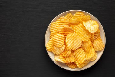 Barbeque Potato Chips on a plate on a black background, top view. Flat lay, overhead, from above. Copy space.