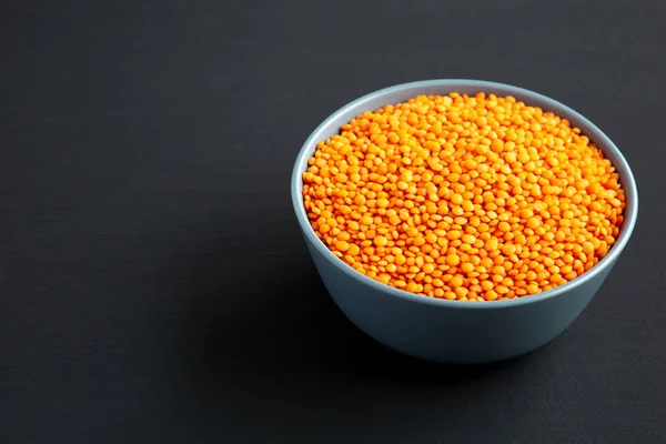 Red Lentils Legume in a Bowl on a black surface, low angle view. Copy space.