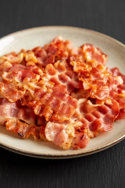 Siyah arka planda, bir tabakta yağlı pastırma, yan görünüm.