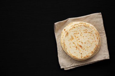 Siyah arka planda tam buğday unlu tortilla yığını, üst manzara. Dümdüz, tepeden, yukarıdan. Boşluğu kopyala.