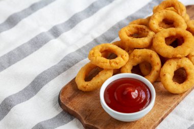 Ev yapımı kızarmış soğan halkaları, yanında ketçap ve ahşap tahta, düşük açılı. Boşluğu kopyala.