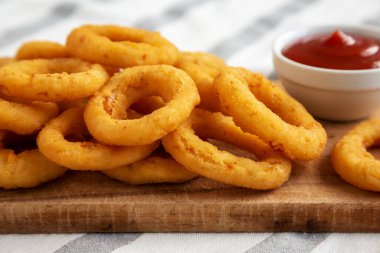 Ev yapımı kızarmış soğan halkaları, yanında ketçap ve ahşap tahta, düşük açılı. Yakın plan..