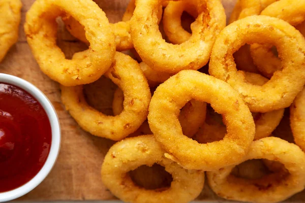 stock image Homemade Crispy Deep-Fried Onion Rings with Ketchup on a rustic wooden board, top view. Flat lay. Close-up.