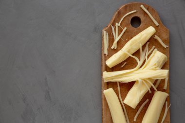 Kırsal bir tahta üzerinde organik String Cheese, gri bir arka plan, üst manzara. Dümdüz, tepeden, yukarıdan. Boşluğu kopyala.