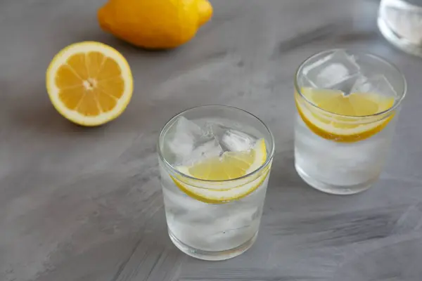 stock image Refreshing Cold Water with Lemon in Glasses on gray background, side view.