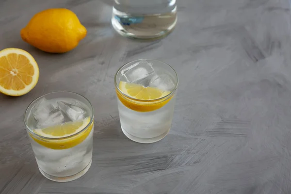 stock image Refreshing Cold Water with Lemon in Glasses on gray background, side view. Copy space.