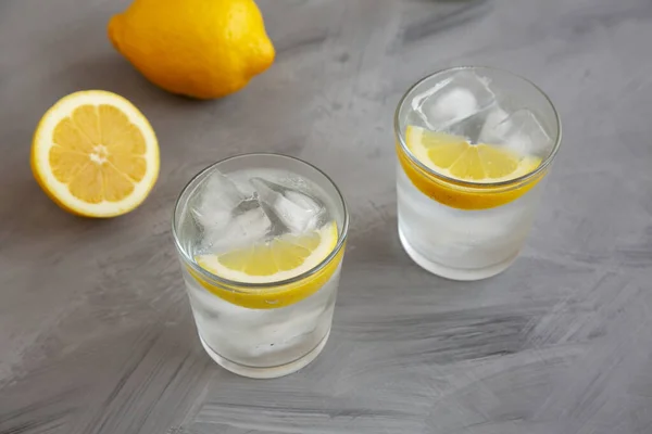 Stock image Refreshing Cold Water with Lemon in Glasses on gray background, side view.