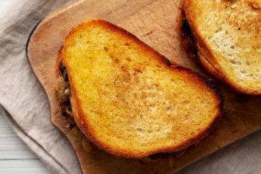 Ev yapımı Fransız eritilmiş sandviçi, karamelli soğan ve rendelenmiş peynirli, ahşap bir tahtanın üstünde. Dümdüz, tepeden, yukarıdan. 