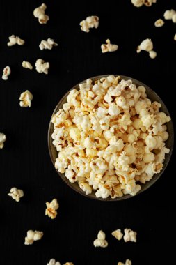 Siyah arka planda Salt in a Bowl ile ev yapımı tereyağlı patlamış mısır. Dümdüz, tepeden, yukarıdan. 