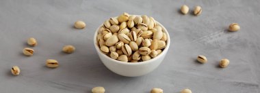 Tuzlu ve kavrulmuş Pistachio 'lar gri arka planda, yan manzaralı bir kasede.