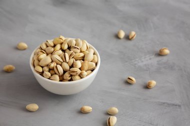 Tuzlu ve kavrulmuş Pistachio 'lar gri arka planda, yan manzaralı bir kasede.