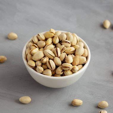 Tuzlu ve kavrulmuş Pistachio 'lar gri arka planda, yan manzaralı bir kasede.