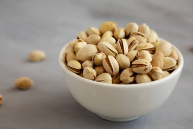 Tuzlu ve kavrulmuş Pistachio 'lar gri arka planda, yan manzaralı bir kasede. 