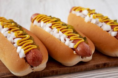 Char ızgara sosisli, hardallı, çeşnili ve soğanlı, ahşap bir tahta üzerinde, yan manzara. Yakın plan..