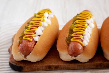 Char ızgara sosisli, hardallı, çeşnili ve soğanlı, ahşap bir tahta üzerinde, yan manzara. Yakın plan..