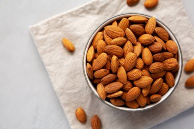 Gri arka planda bir kasede çiğ organik badem, üst görünüm. 