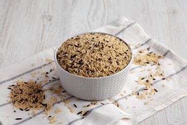 Beyaz ahşap arka planda bir kasede çiğ organik yaban pirinci..