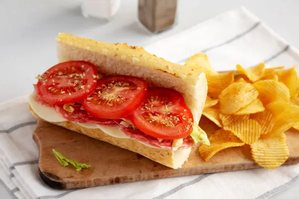 stock image Homemade Italian Sub Sandwich with Salami, Tomatoes and Shredded Iceberg Lettuce on a rustic wooden board, side view.