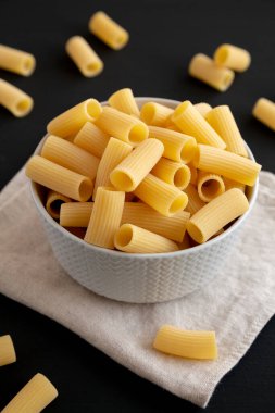 Kuru Rigatoni Makarnası siyah arka planda bir kasede, yan görünümde..