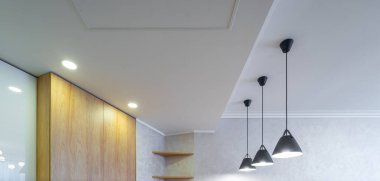 Modern light interior. White ceiling. Black lamps. Wooden cabinets and shelves.