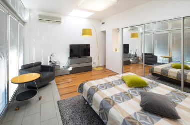 Lüks bir dairede, aydınlık yatak odasının modern iç mekanı. Ayna kapılı gardırop. Sıcak yatak. TV.