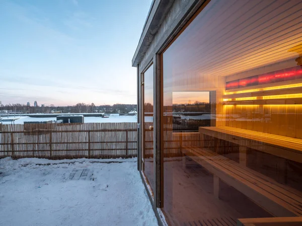 Small wooden finnish sauna with glass door on terrace of cottage. Luxury private house.