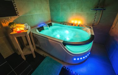 Lüks banyonun modern iç mekanı. Suyla aydınlatılmış masaj banyosu. Mumlar. Romantik atmosfer.