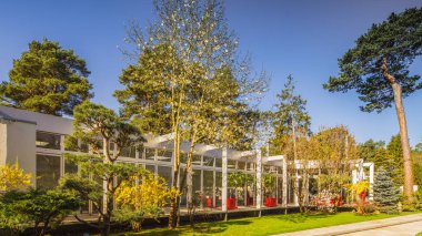 Lüks özel evin modern dış cephesi. Güneşli bir yaz günü. Cam duvar. Bahçedeki güzel ağaçlar.